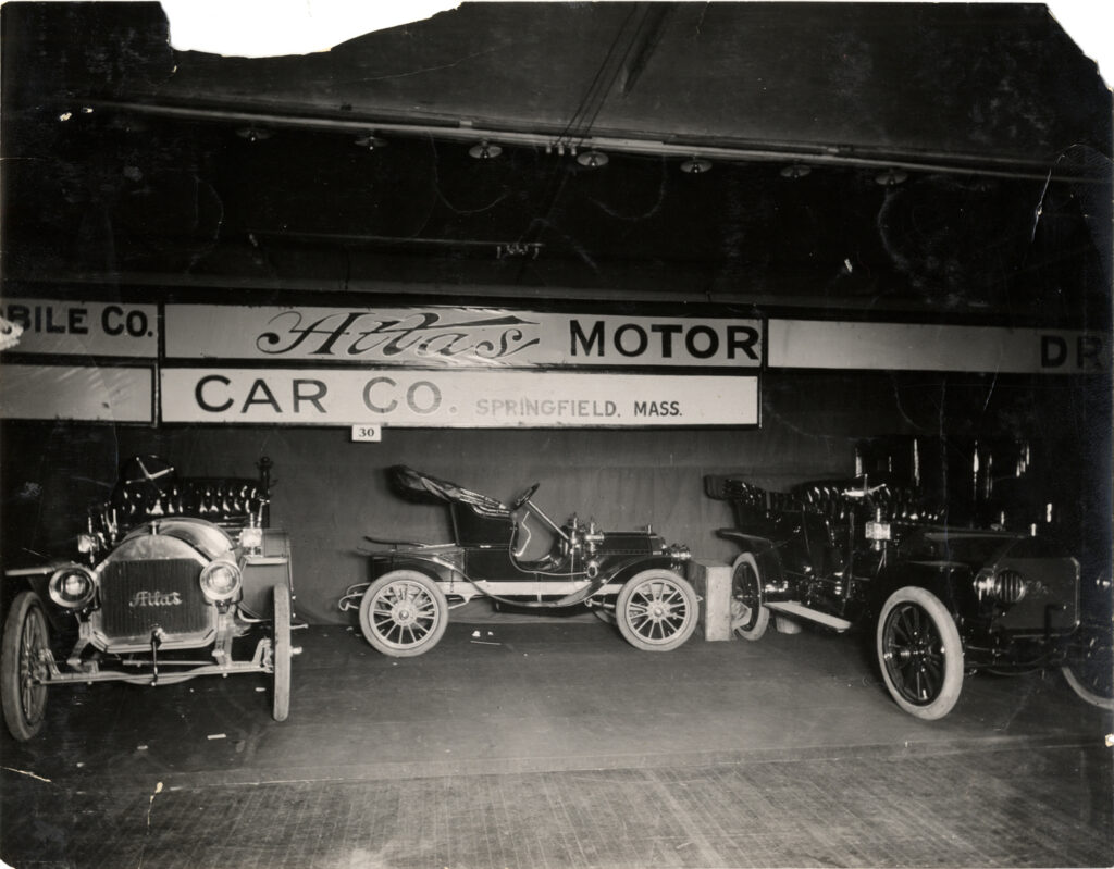 View of 1908 Atlas cars on display at trade show. "Atlas Motor car Co., Springfield, Mass." sign is displayed in background. (source: National Automotive History Collection, Detroit Public Library.)